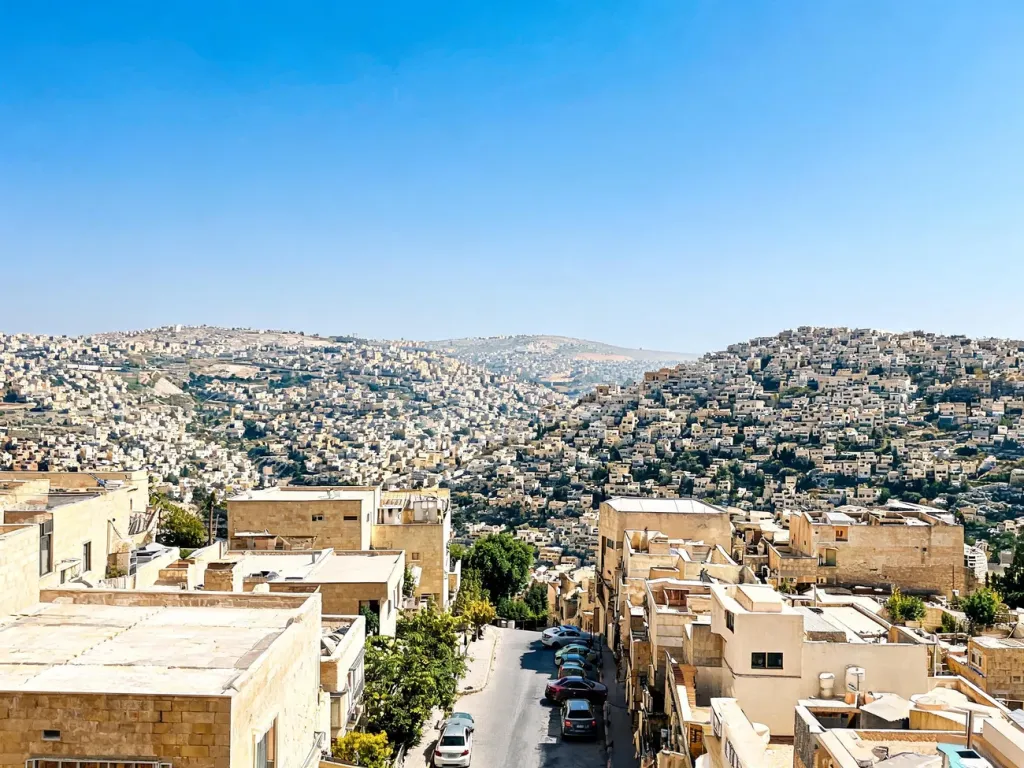 Panorama Amman za dnia z zabudową na wzgórzach, jasne piaskowe budynki i wąskie uliczki pod błękitnym niebem